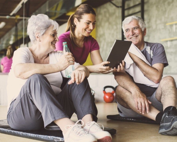 An Older Couple & a Younger Woman Sit Together on a Fitness Center Floor in CO