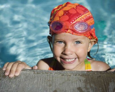 A girl swims in a pool under the sun, enjoying a warm day at Wellbridge Athletic Club