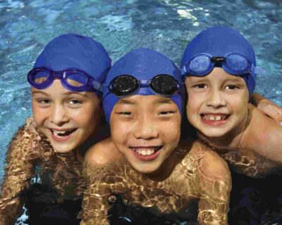 Three children in swim caps and goggles play in the swimming pool, Albuquerque, NM