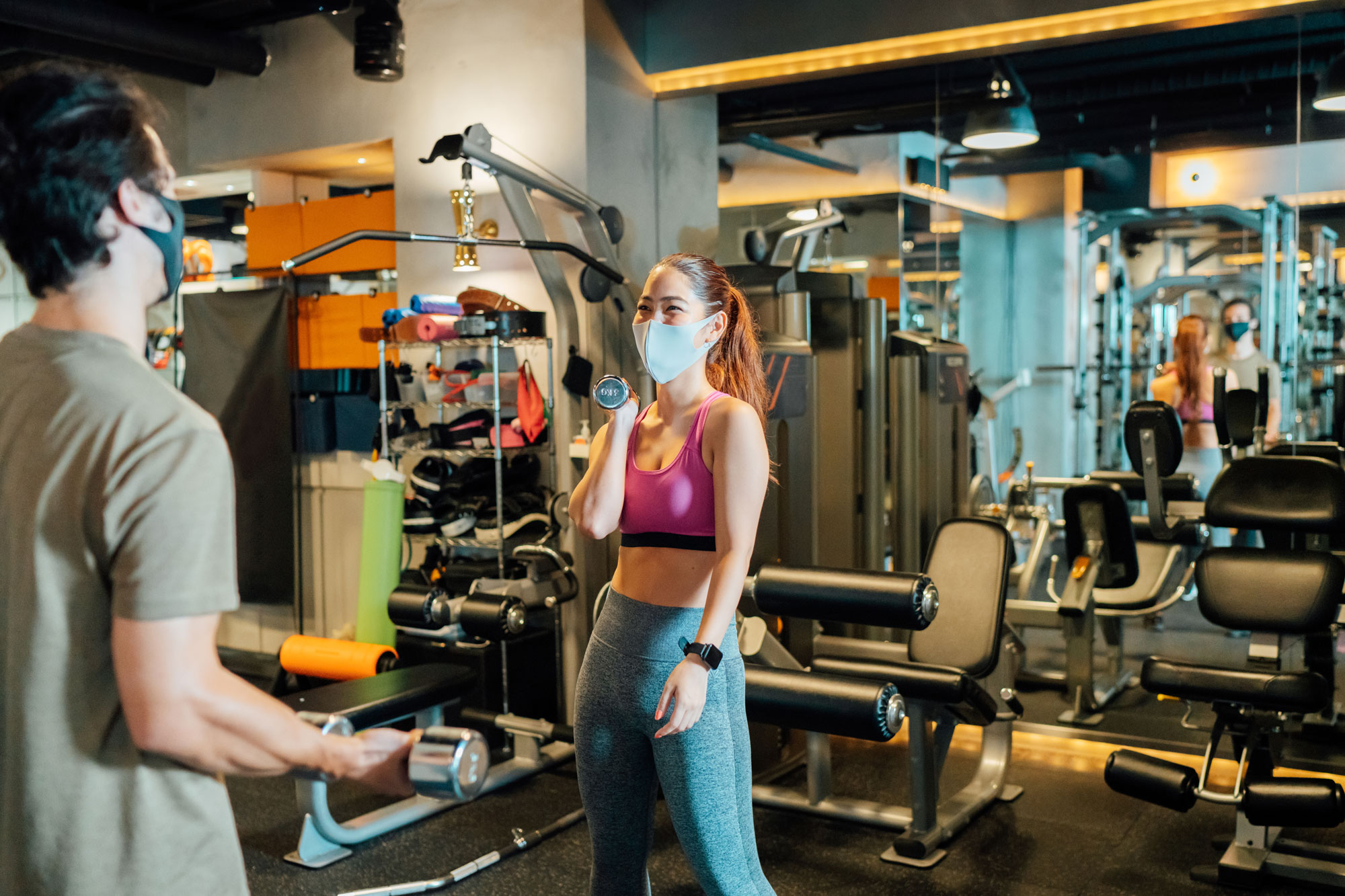 Man and woman working out in the gym wearing masks