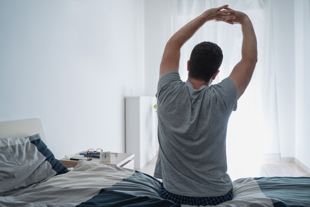 Man stretches muscles on the bed in the bedroom in the morning