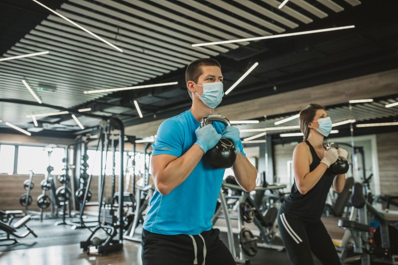 Masked couple working out with kettlebells at Wellbridge